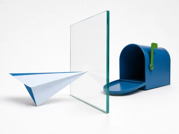 A paper airplane stopped by a glass barrier before reaching an open mailbox